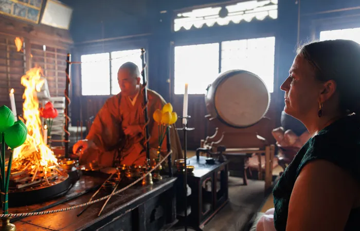 A monk performs a goma fire ritual, with bright flames rising from the altar to evoke purification and inner warmth.