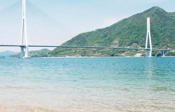 The Seto Ohashi Bridge stretches across calm blue waters with mountains rising in the background, reflecting the serene island landscape of Setouchi.